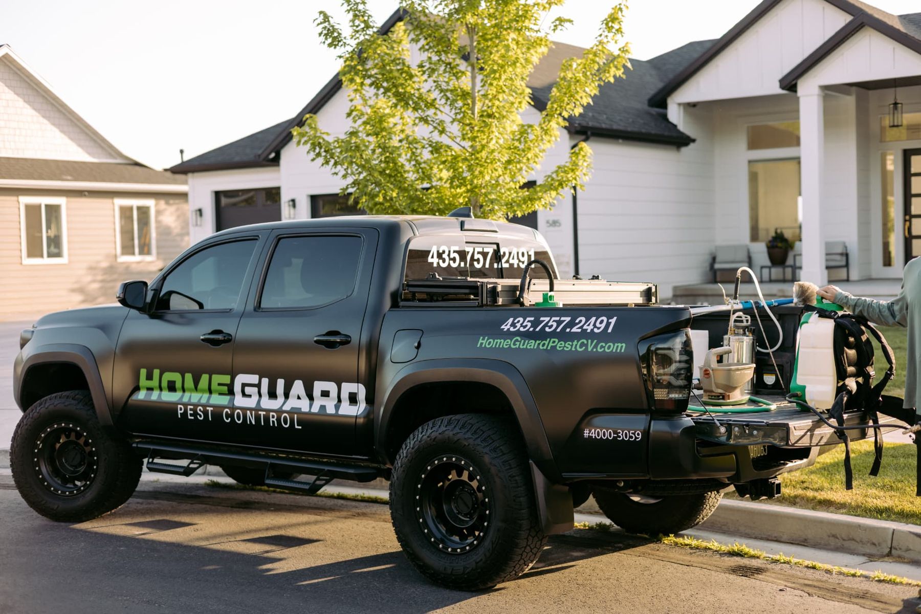 Wrapped black HomeGuard Pest Control truck with equipment on the tailgate