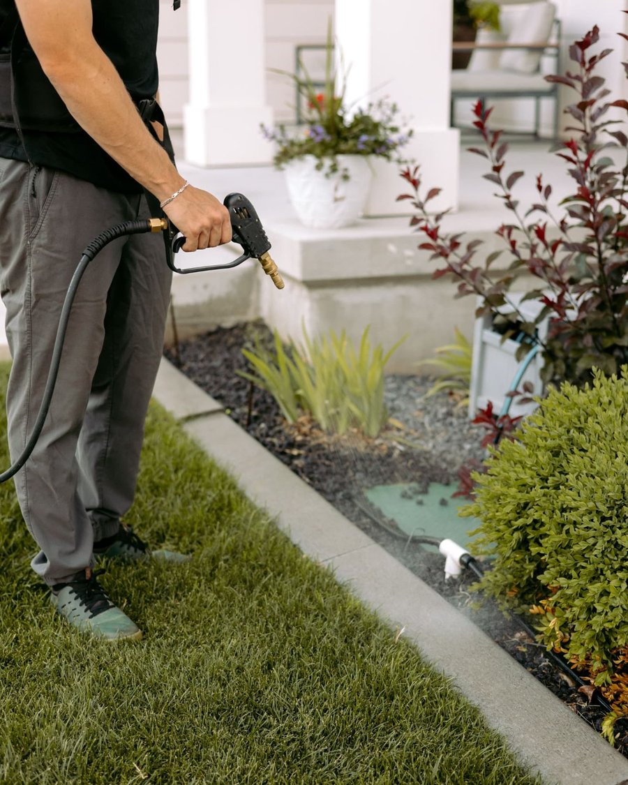 HomeGuard technician spraying along a home foundation and flower bed